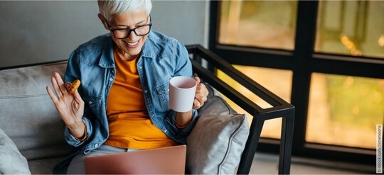 Frau mit entspanntem und glücklichen Gesichtsausdruck am Laptop und mit einer Tasse Tee in der Hand, die online in einer Selbsthilfegruppe zum Thema Blasenbeschwerden unterwegs ist